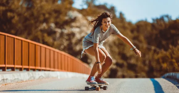Jeune femme fait du skateboard sur une route ensoleillée